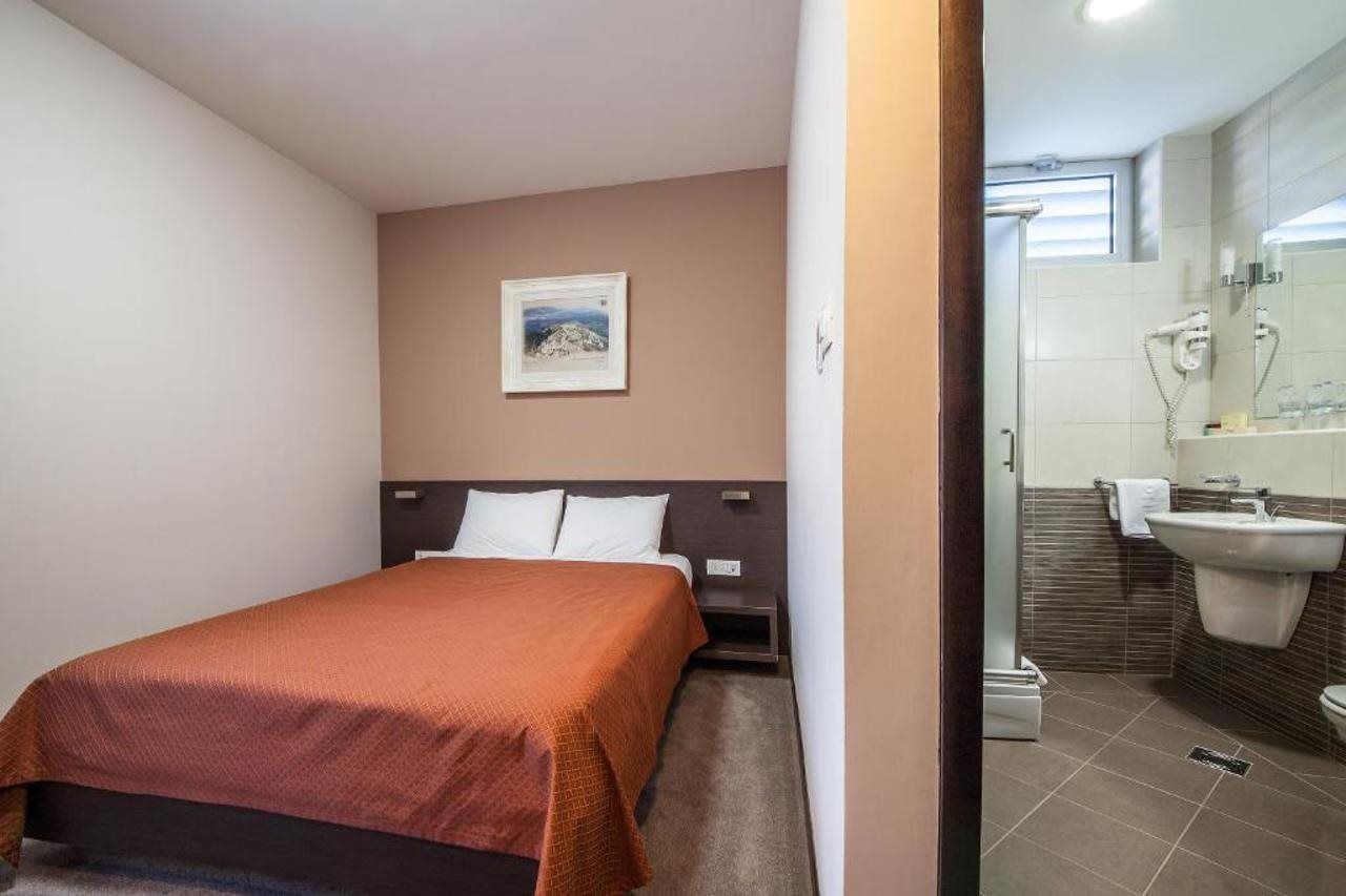 A hotel room with a bed, a nightstand, a wall-mounted picture, and a bathroom with a sink and mirror.