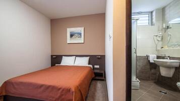 A hotel room with a bed, a nightstand, a wall-mounted picture, and a bathroom with a sink and mirror.