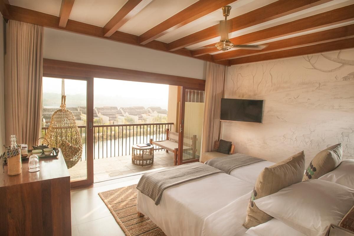 A bedroom with two beds, a TV, a balcony with a view, and a wooden ceiling.