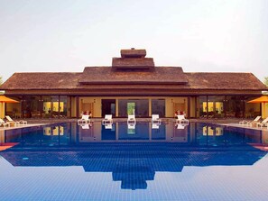 A resort with a large swimming pool, lounge chairs, and a thatched-roof building.