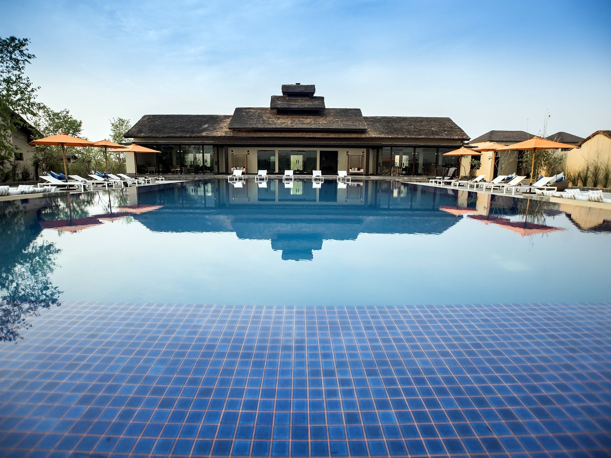 Una piscina con sillas de descanso y sombrillas, rodeada de edificios de estilo arquitectónico moderno.