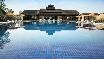 Una piscina con sillas de descanso y sombrillas, rodeada de edificios de estilo arquitectónico moderno.