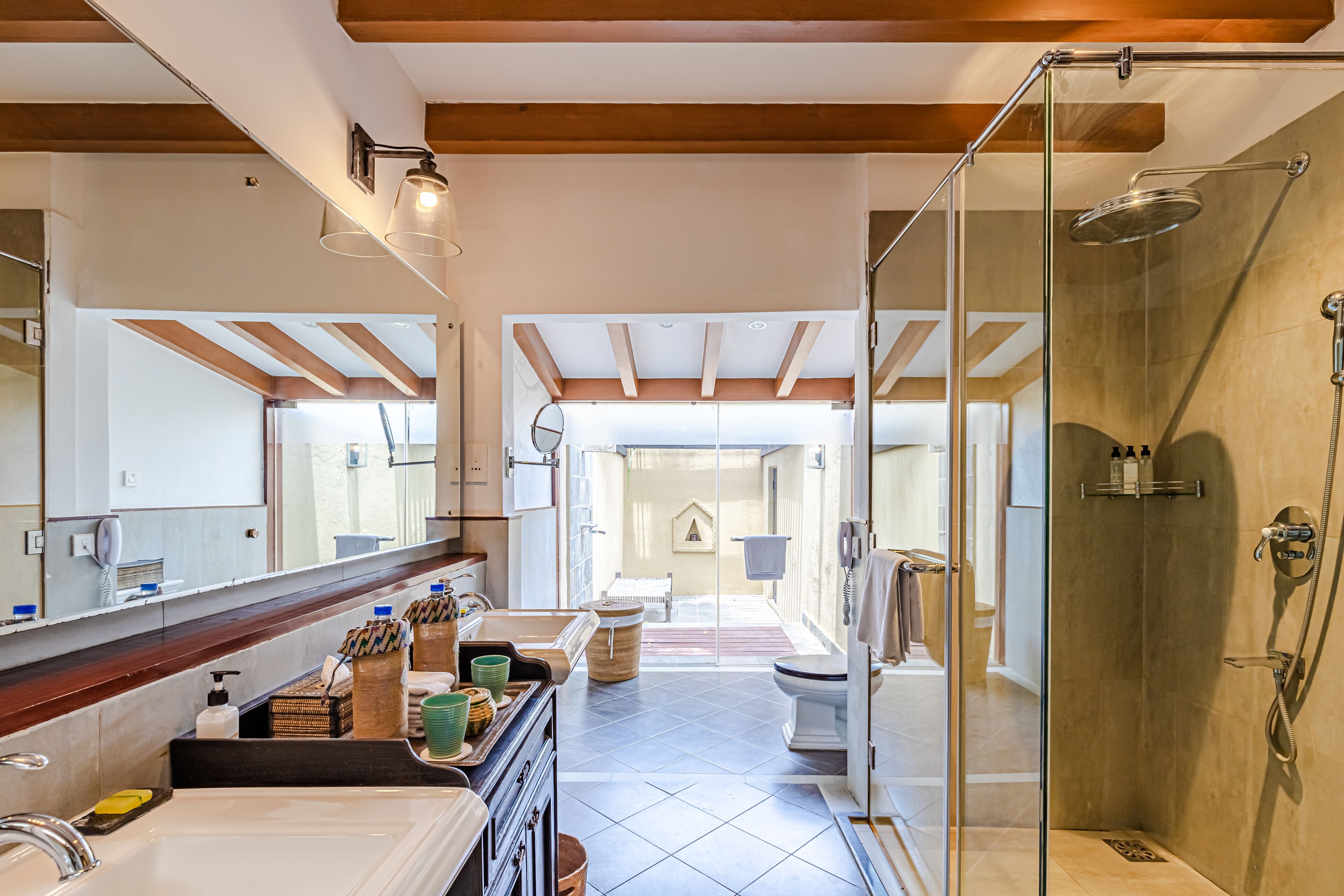A modern bathroom with a glass-enclosed shower, a large mirror, and a vanity with toiletries.