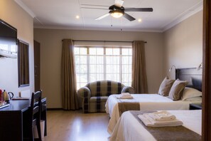A hotel room with two beds, a desk, a chair, a ceiling fan, and a window with curtains.