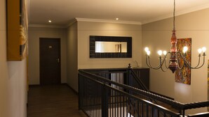 A hallway with a staircase, a door labeled "28", a wall-mounted mirror, and a chandelier. - Ruth Avenue Guest House (Edenvale)