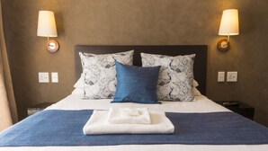 A neatly made bed with patterned pillows, a folded towel, and two wall-mounted lamps. - Ruth Avenue Guest House (Edenvale)