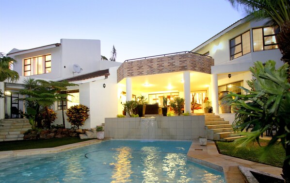 A modern house with a swimming pool, a covered patio, and a well-maintained garden.