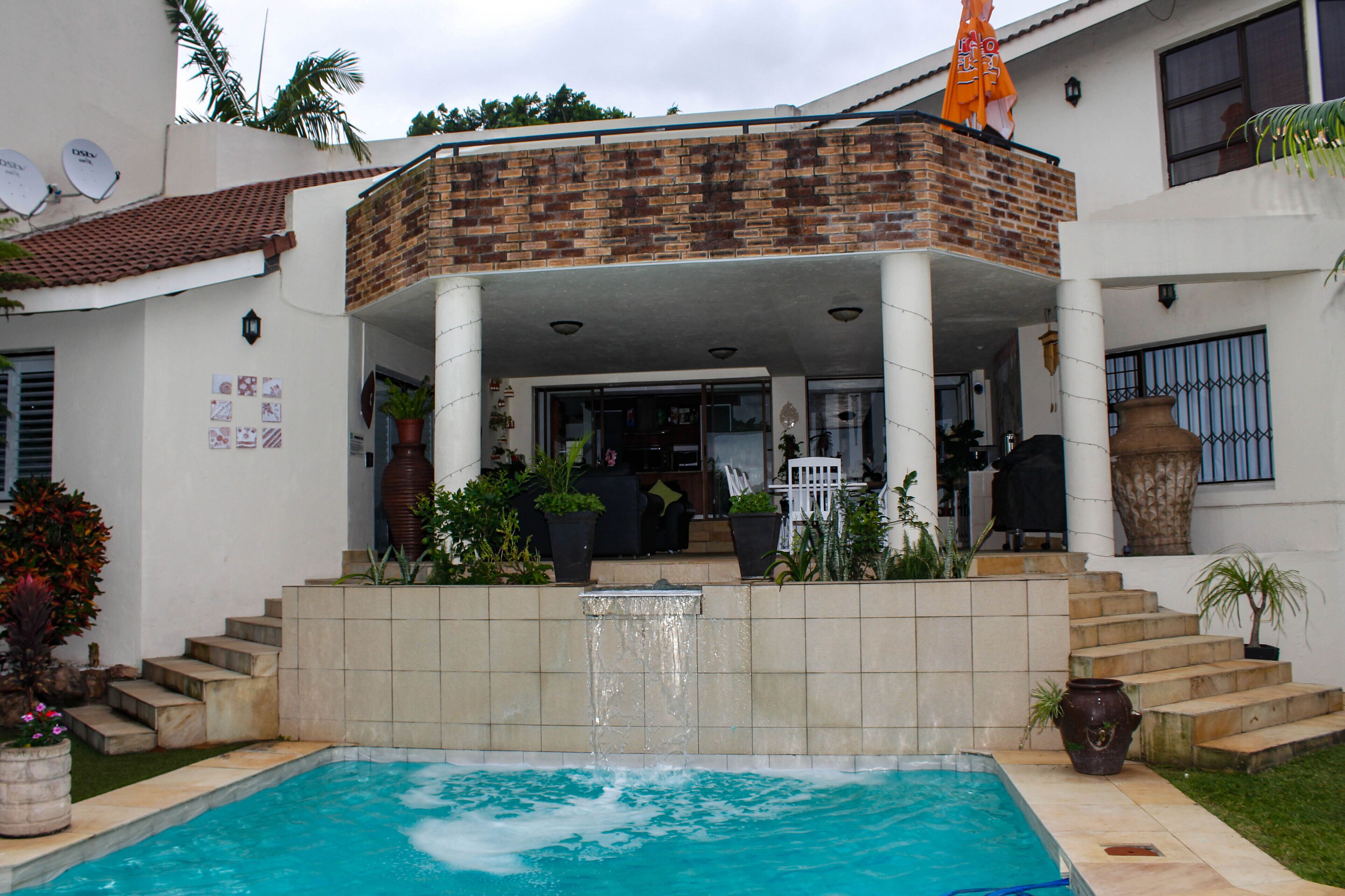 Une maison à deux étages dotée d’une piscine, d’un patio couvert et d’une façade en briques.
