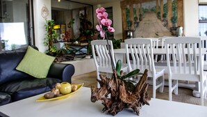 A living room with a white coffee table, a sofa, and a dining area with white chairs.
