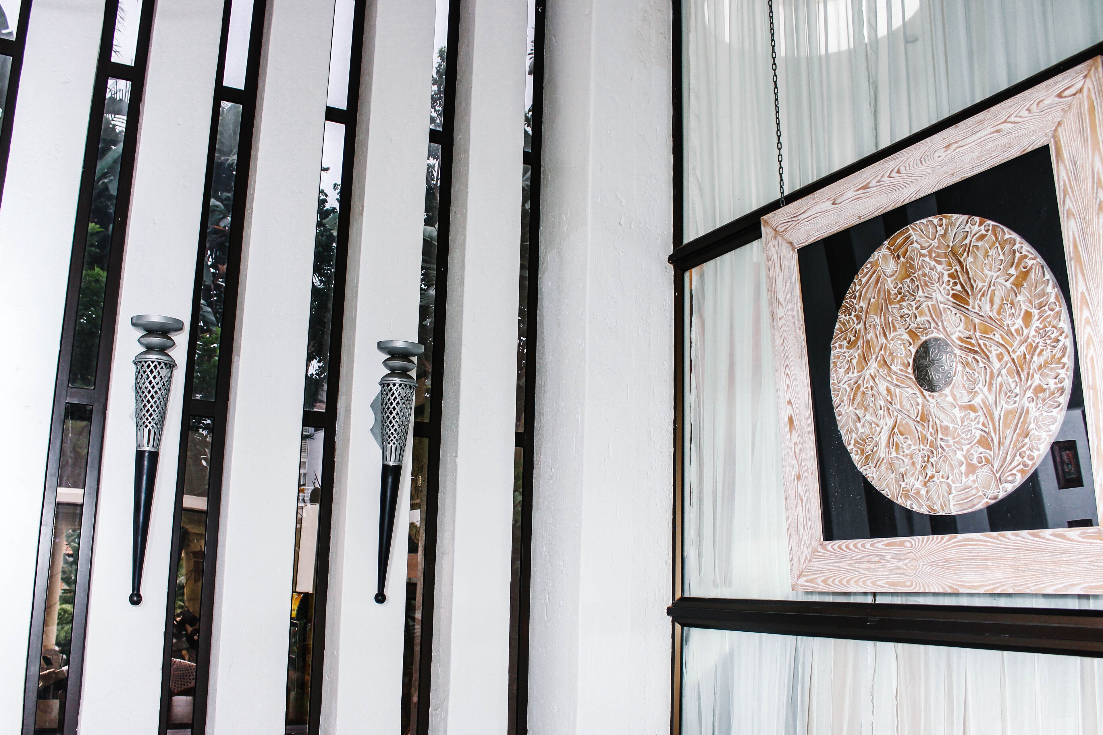 A room with a large window, a decorative circular mirror, and a black and white striped pattern on the wall.