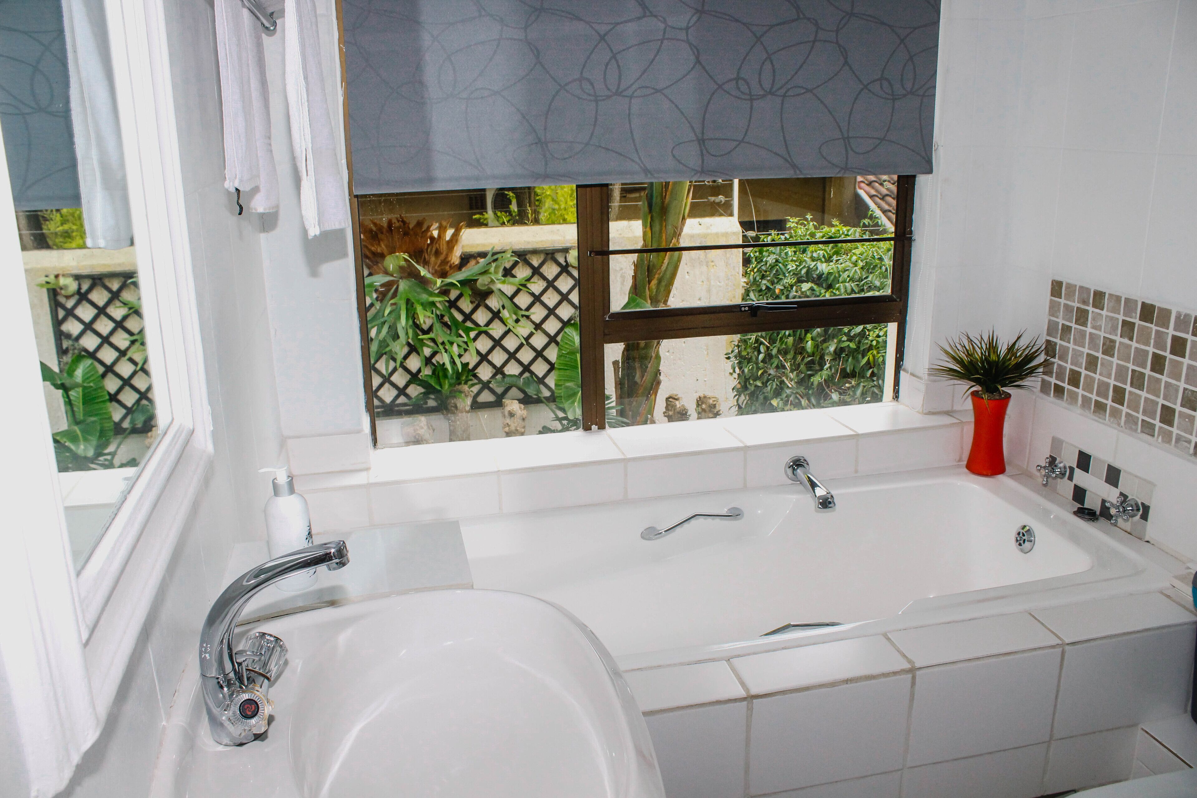 A bathroom with a large bathtub, a window with a view of greenery, and a potted plant.