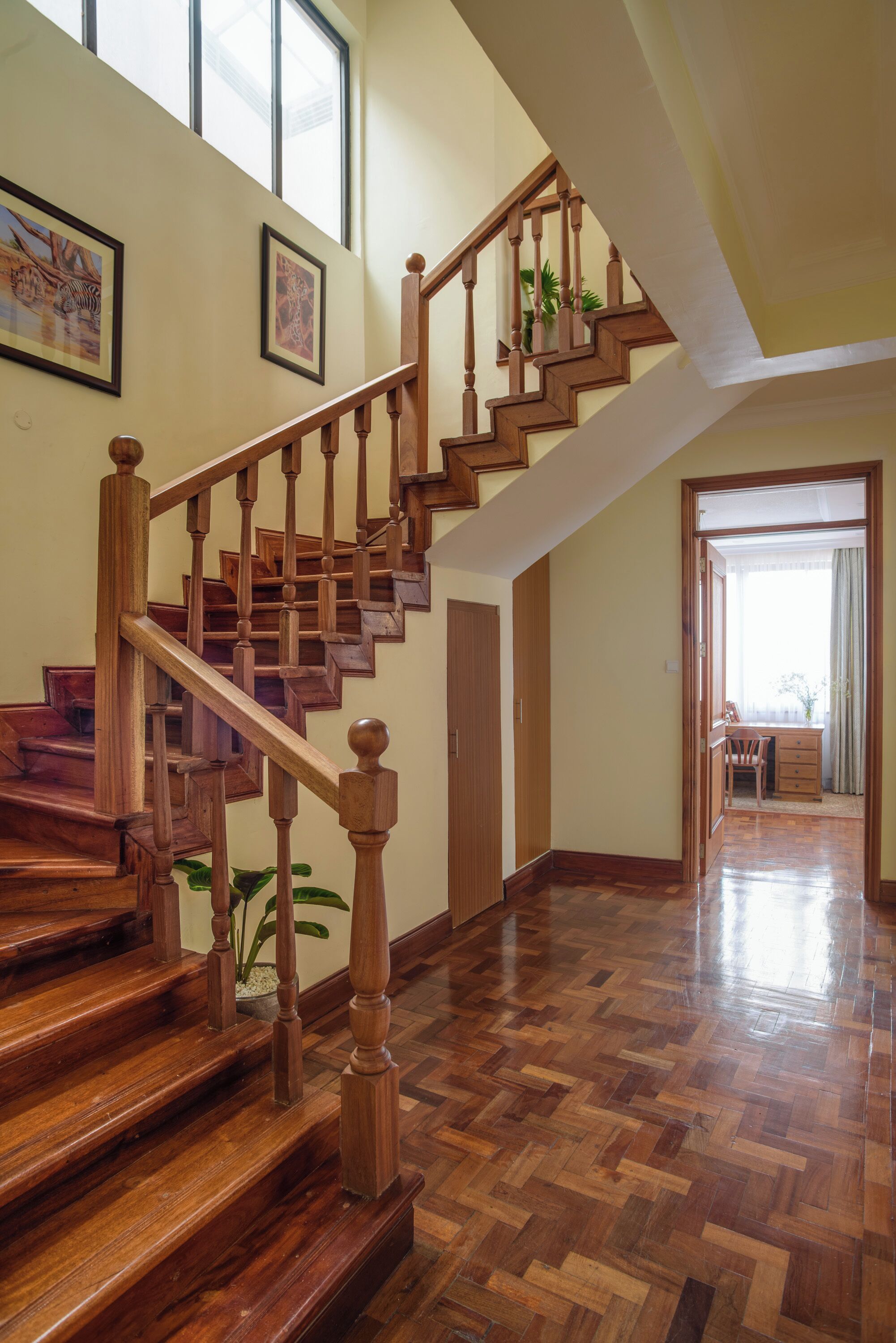 A wooden staircase with a handrail, leading to a room with a herringbone floor pattern.
