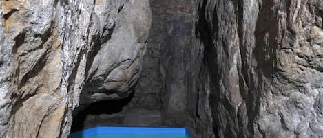 Una estructura estrecha y rocosa, similar a una cueva, con una piscina rectangular al final.