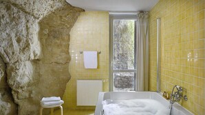 Een badkamer met een groot bad vol bubbels, een stenen muur en gele betegelde wanden.