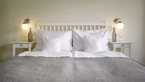 Ein ordentlich bezogenes Bett mit weißen Leinen und Kissen, begleitet von zwei Nachttischen mit Lampen und Flaschen.