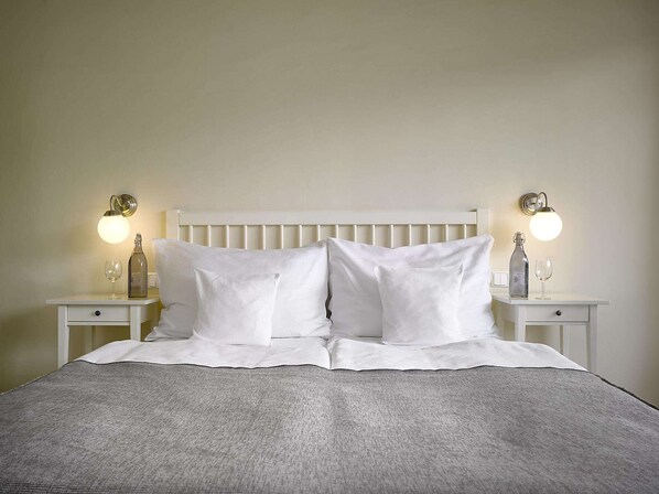 A neatly made bed with white linens and pillows, flanked by two bedside tables with lamps and bottles. - Hotel La Romantica (Mlada Boleslav)
