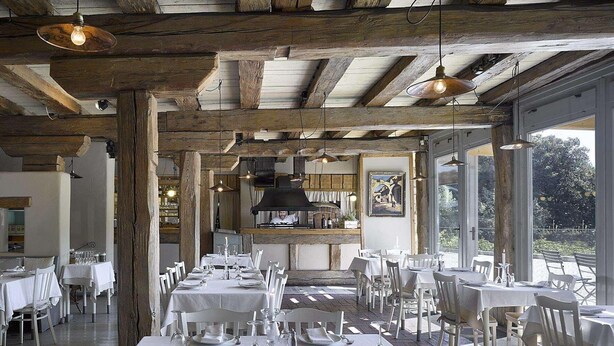 Ein Restaurant mit Holzbalken, weißen Tischen und Blick ins Freie.