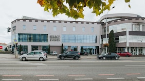 A building with a 'Select Events' sign, multiple cars parked in front, and a pedestrian crossing. - Hotel Select (Sibiu)