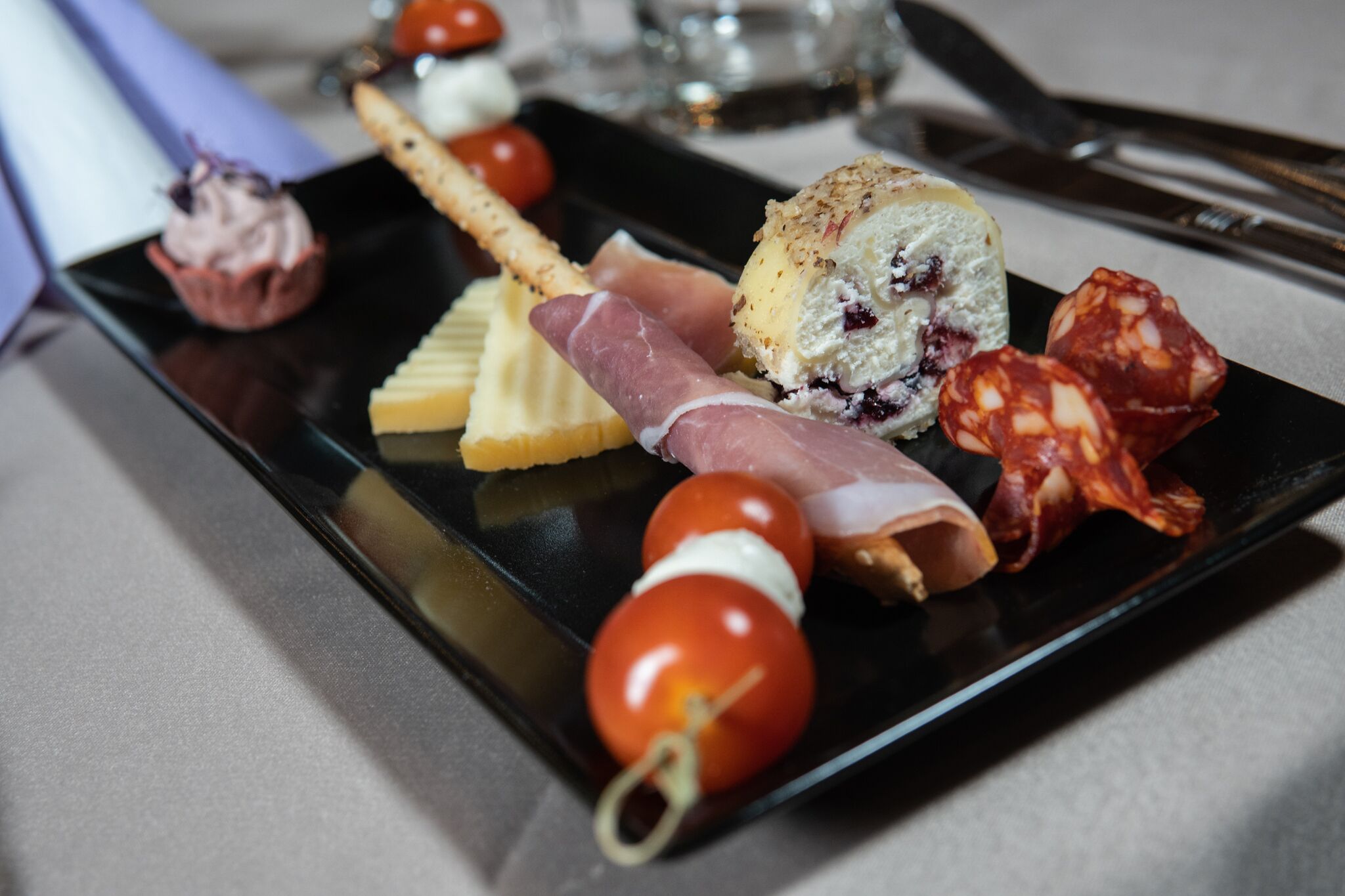 A black rectangular plate with various food items including cheese, meat, and cherry tomatoes.