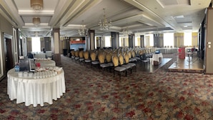 A banquet hall with rows of chairs, a buffet table with plates and cups, and a stage with a podium. - Hotel Select (Sibiu)