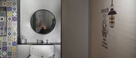 A bathroom with a white sink, a round mirror, and a wall with a hexagonal pattern.