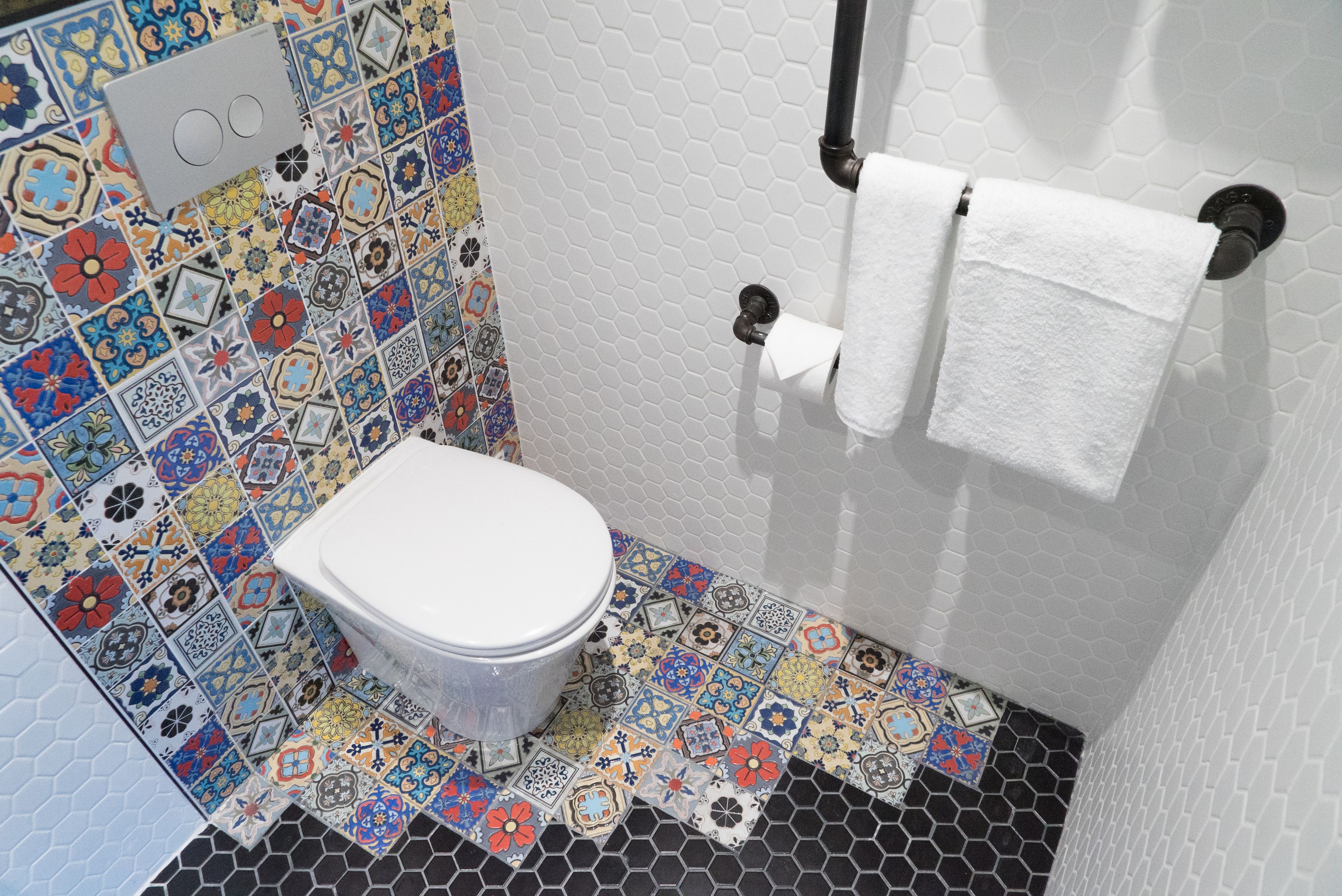 A bathroom with a toilet, a toilet paper holder, and a towel rack. The walls are tiled with a mix of colorful and patterned tiles.