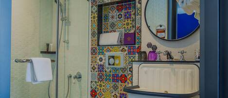 Un baño con ducha, inodoro, lavamanos y una pared de azulejos de colores.