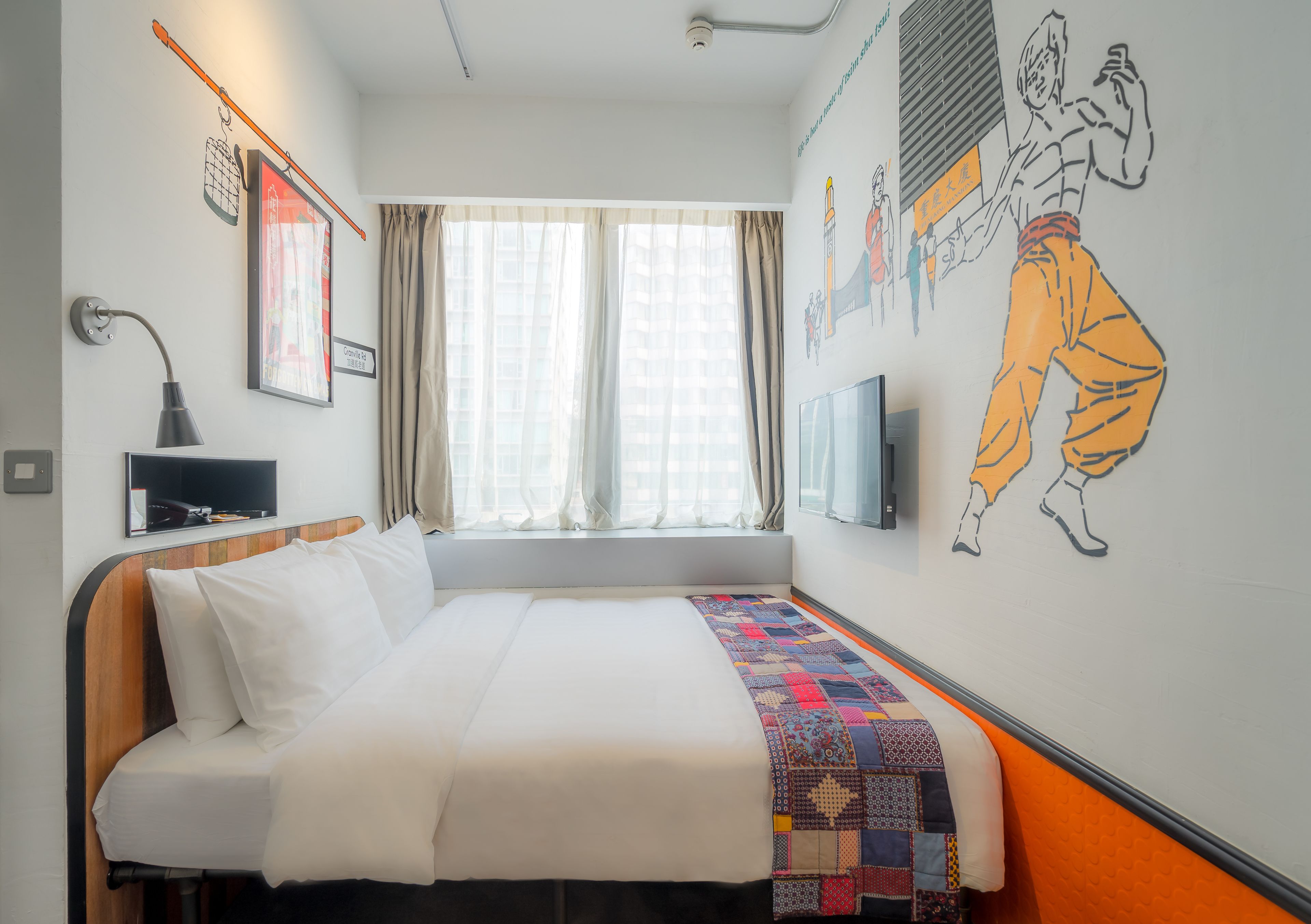 A hotel room with a bed, a TV, a window with curtains, and a wall with artwork.
