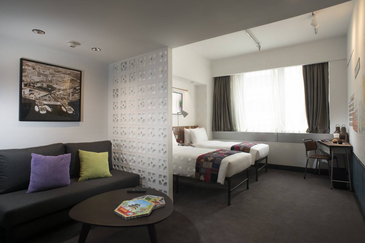 A hotel room with a sofa, two beds, a desk, and a window with curtains.