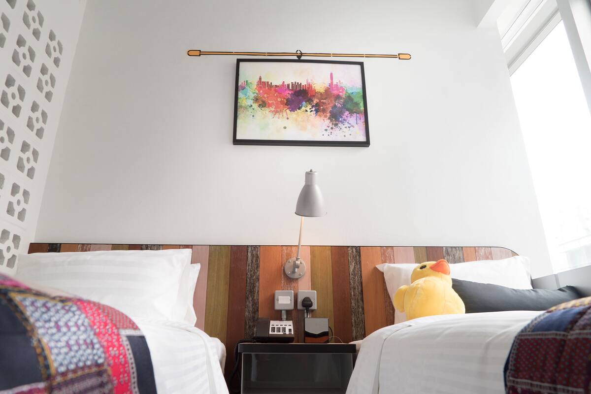 A hotel room with a bed, a bedside table with a lamp, a wall-mounted picture, and a window.