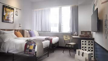 Habitación de hotel con dos camas, un escritorio, una silla, un televisor y una ventana con cortinas.