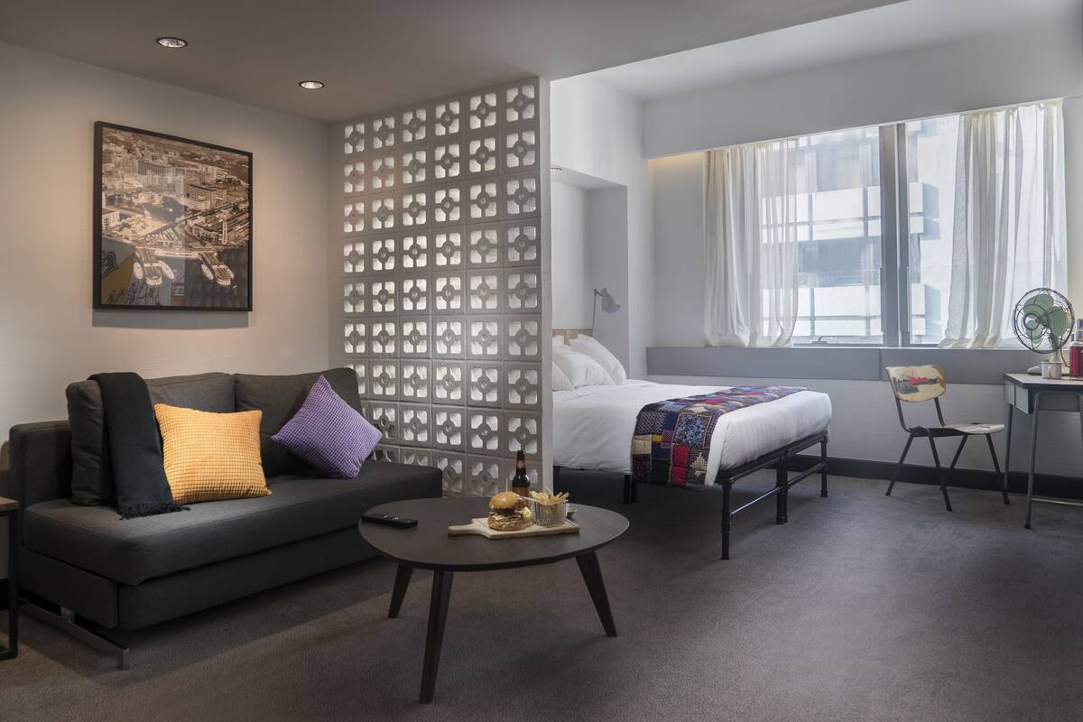 A modern hotel room with a sofa, a bed, a desk, and a window with curtains.