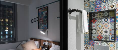 A hotel room with a bed, bedside table, lamp, and a colorful tile wall.