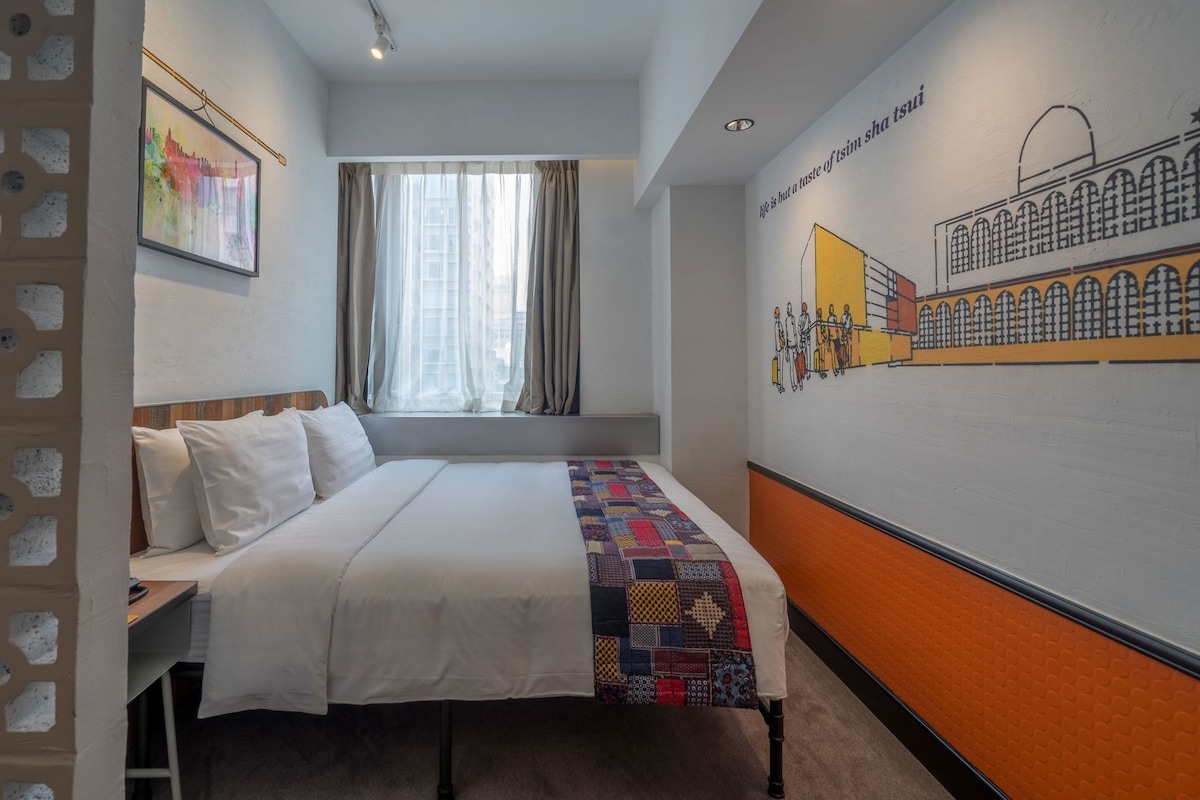 A hotel room with a bed, a window with curtains, a wall mural, and a partial view of a cityscape.