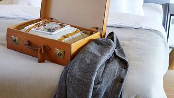 A bed with a suitcase on it, a grey coat draped over the side, and a book on top of the suitcase.