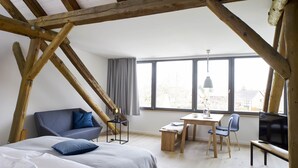 A bedroom with a bed, a desk, and a chair, wooden beams on the ceiling, and large windows. - WohnGut Wolfsburg (Wolfsburg)