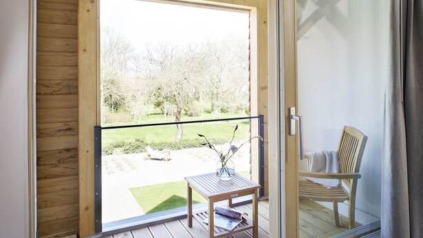 A balcony with a wooden floor, a table with a vase, and a chair. - WohnGut Wolfsburg (Wolfsburg)