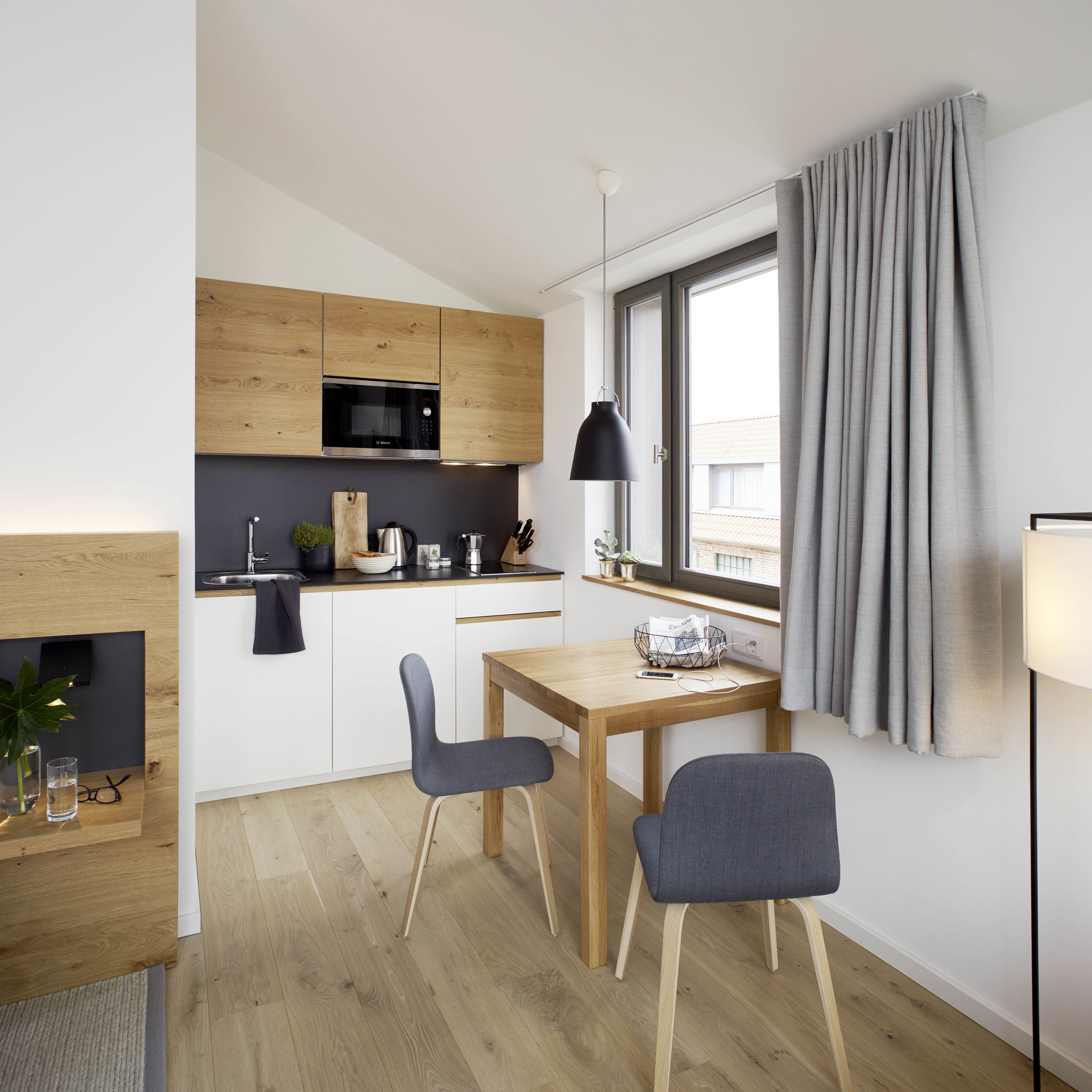 Ett modernt kök med träskåp, en inbyggd mikrovågsugn och en matplats med två stolar och ett bord.