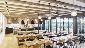 A modern dining area with wooden tables and chairs, a brick wall, and large windows. - WohnGut Wolfsburg (Wolfsburg)