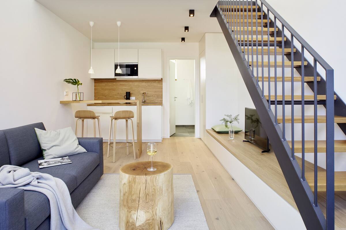 Una sala de estar moderna con un sofá gris, una mesa de centro y una escalera con barandilla de madera.