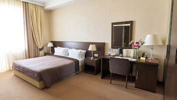 Een hotelkamer met een groot bed, een bureau met stoel, een nachtkastje, een spiegel en een lamp.
