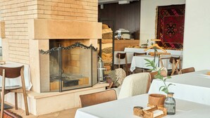 A cozy restaurant with a brick fireplace, wooden chairs, and tables set for dining. - Kainar Hotel (Shymkent)