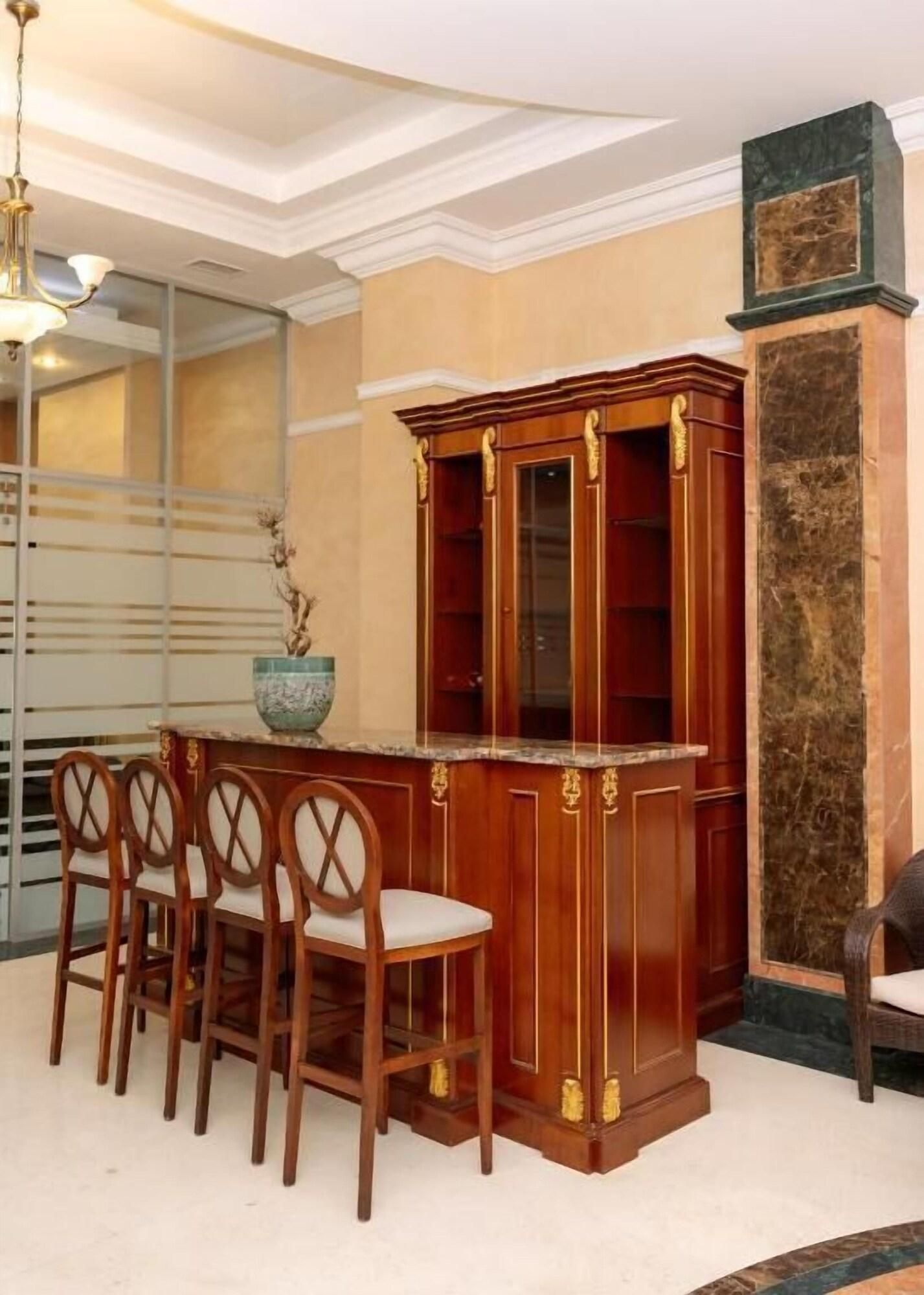 A dining area with a wooden bar and chairs, a vase with flowers, and a decorative column.