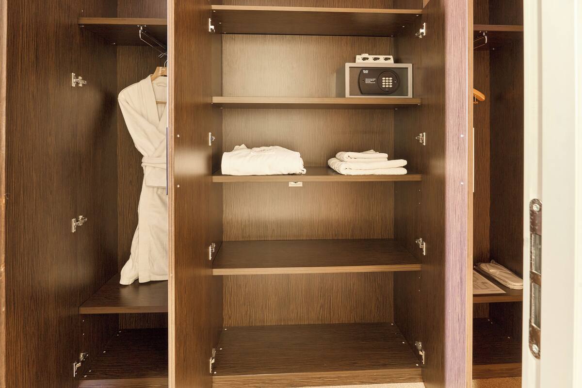 A wooden wardrobe with multiple shelves, a hanging robe, and a safe.