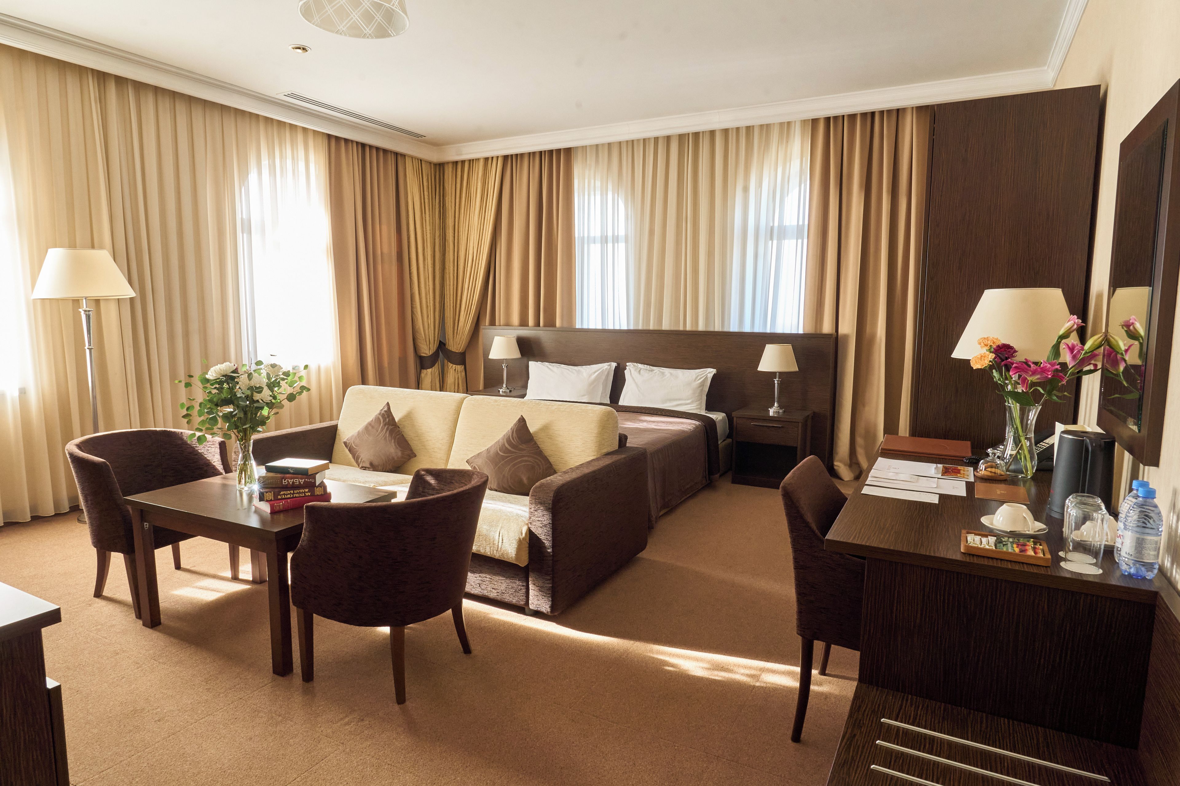 A hotel room with a bed, a desk, a chair, a sofa, and a lamp.