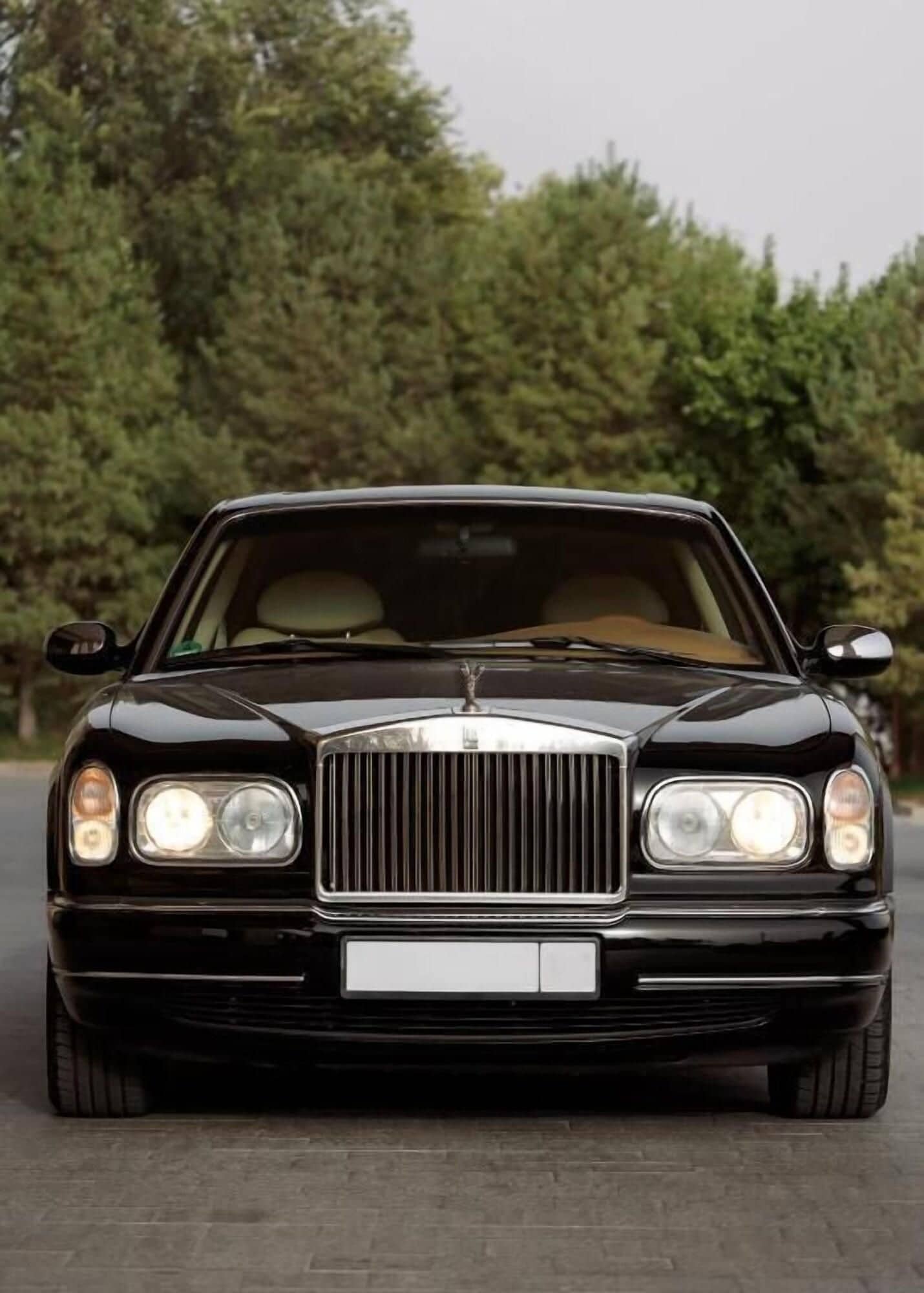 A black luxury car parked on a road with trees in the background.