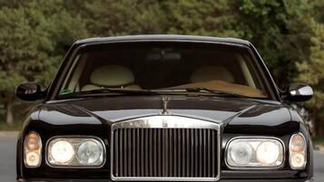 A black luxury car parked on a road with trees in the background.
