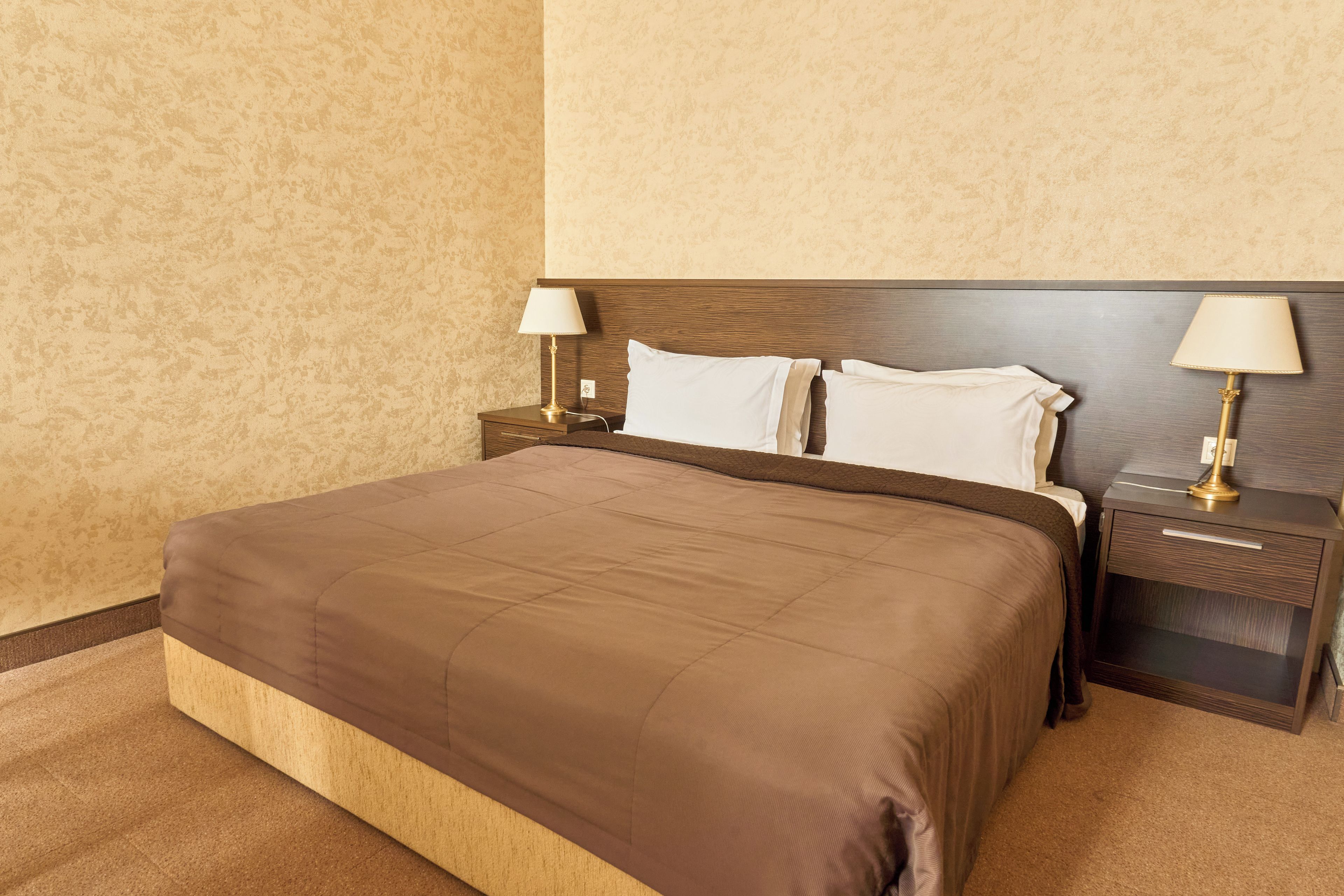 Una camera d'albergo con un letto grande, due comodini con lampade e una testata del letto in legno.