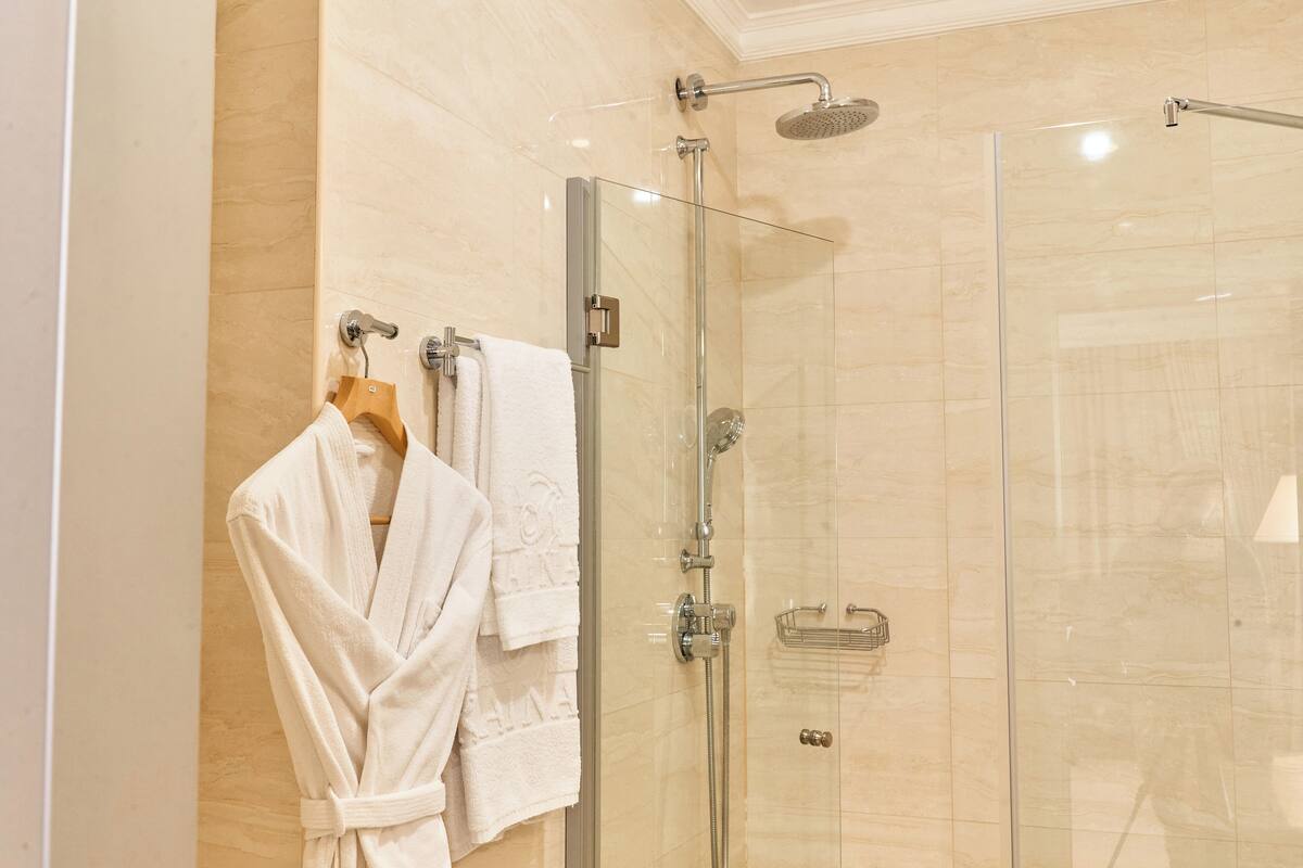 A glass-enclosed shower with a handheld showerhead and a wall-mounted faucet.