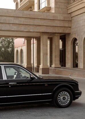 A black luxury car parked in front of a building with classical architecture, including columns and arched windows.